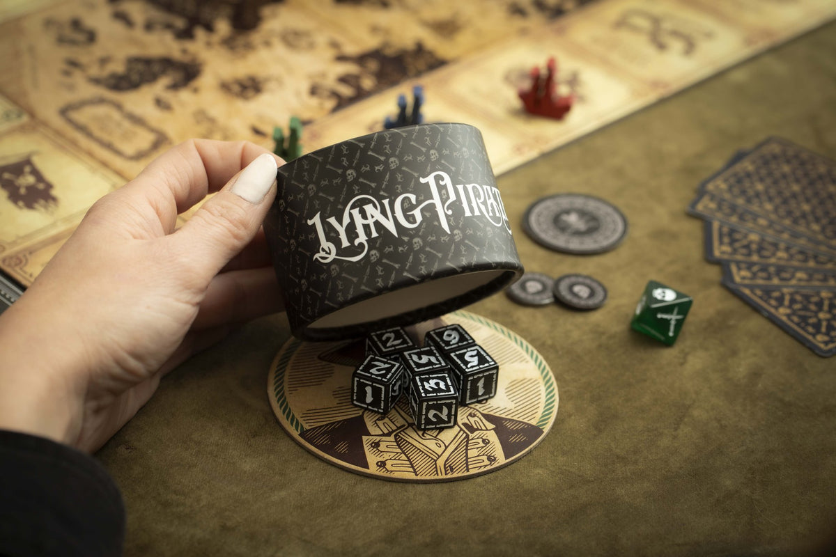 A hand lifting a Lying Pirates dice cup to reveal crew dice on a captain coaster